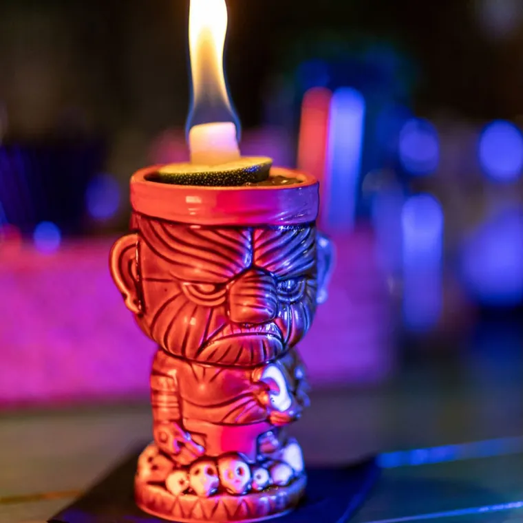 A flaming carved tiki mug cocktail with a lime shell on fire