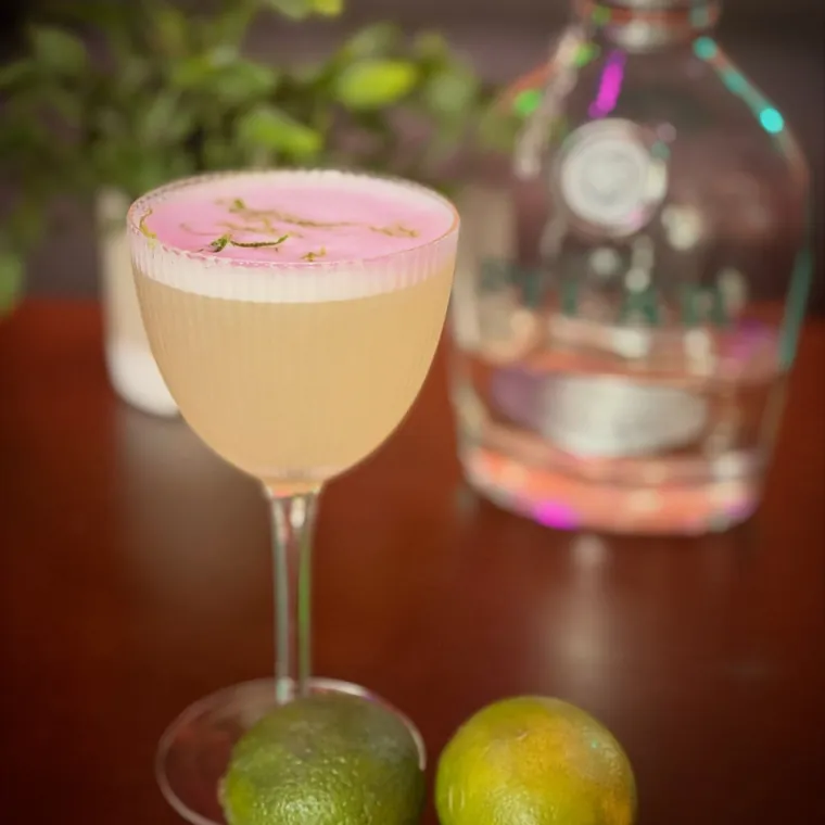 A clean coupe cocktail with fresh limes on a dark bar top