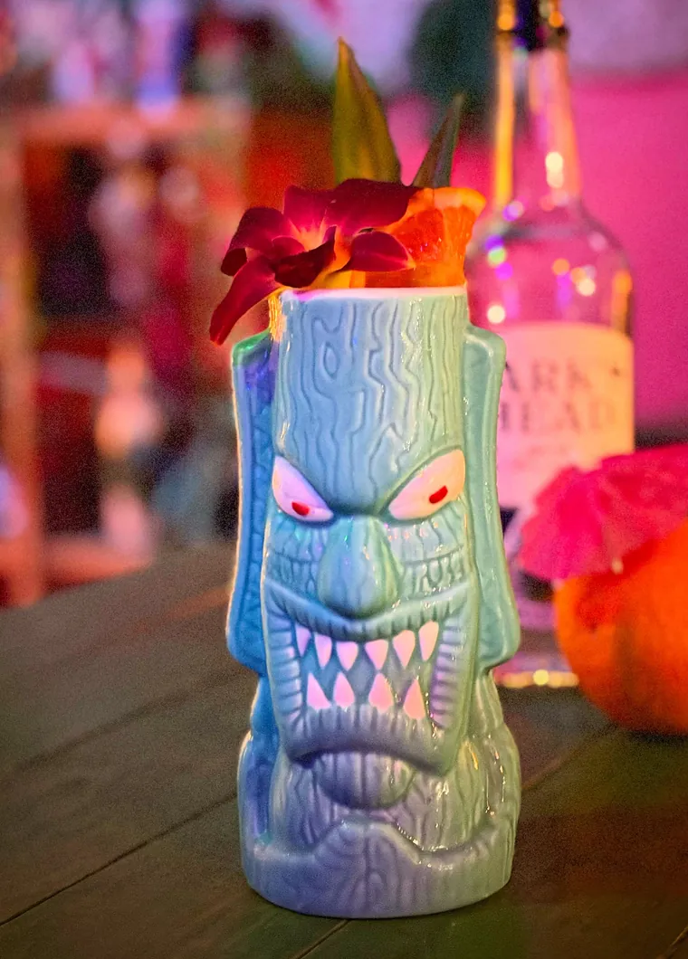 A cocktail served in a carved green monster tiki mug with orchids and a paper parasol at The Tipsy Skipper in Ocala