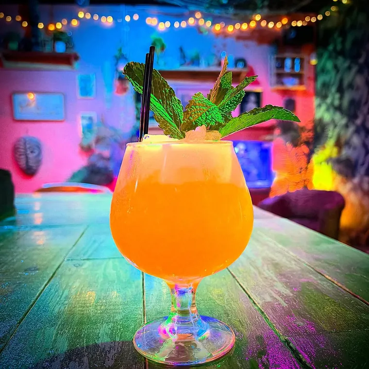 A tall tropical cocktail in a footed goblet under string lights at The Tipsy Skipper in downtown Ocala