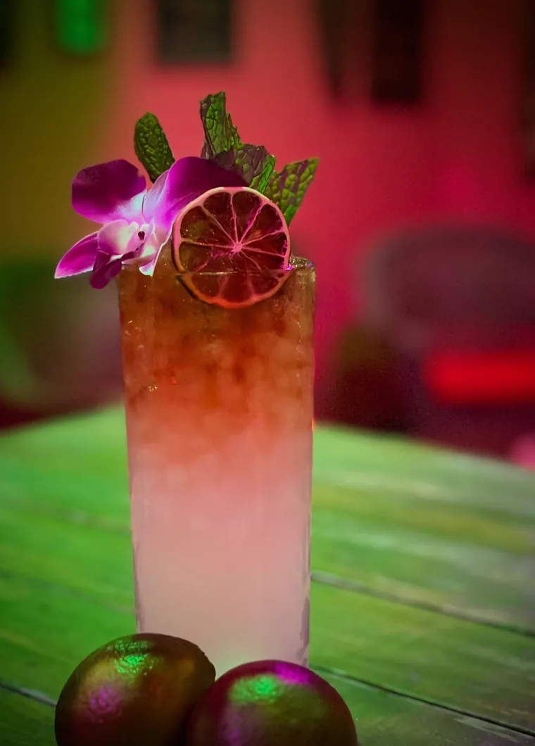 A layered tropical cocktail topped with a fresh orchid and dried citrus wheel