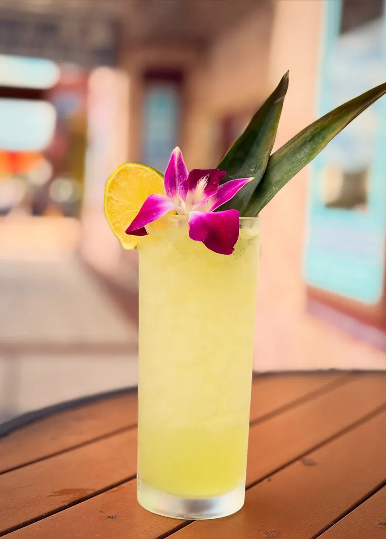 A tall cocktail over crushed ice with an orchid and pineapple frond garnish