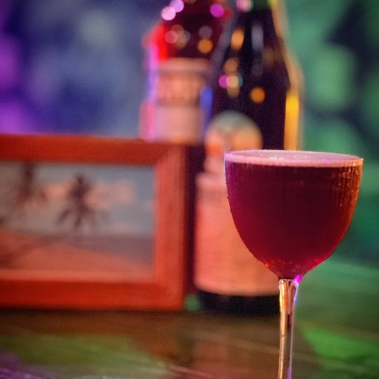 A deep red cocktail served up in a coupe glass under neon at The Tipsy Skipper