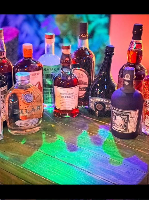 Rare and independent rum bottles lined up on the bar under green and violet light